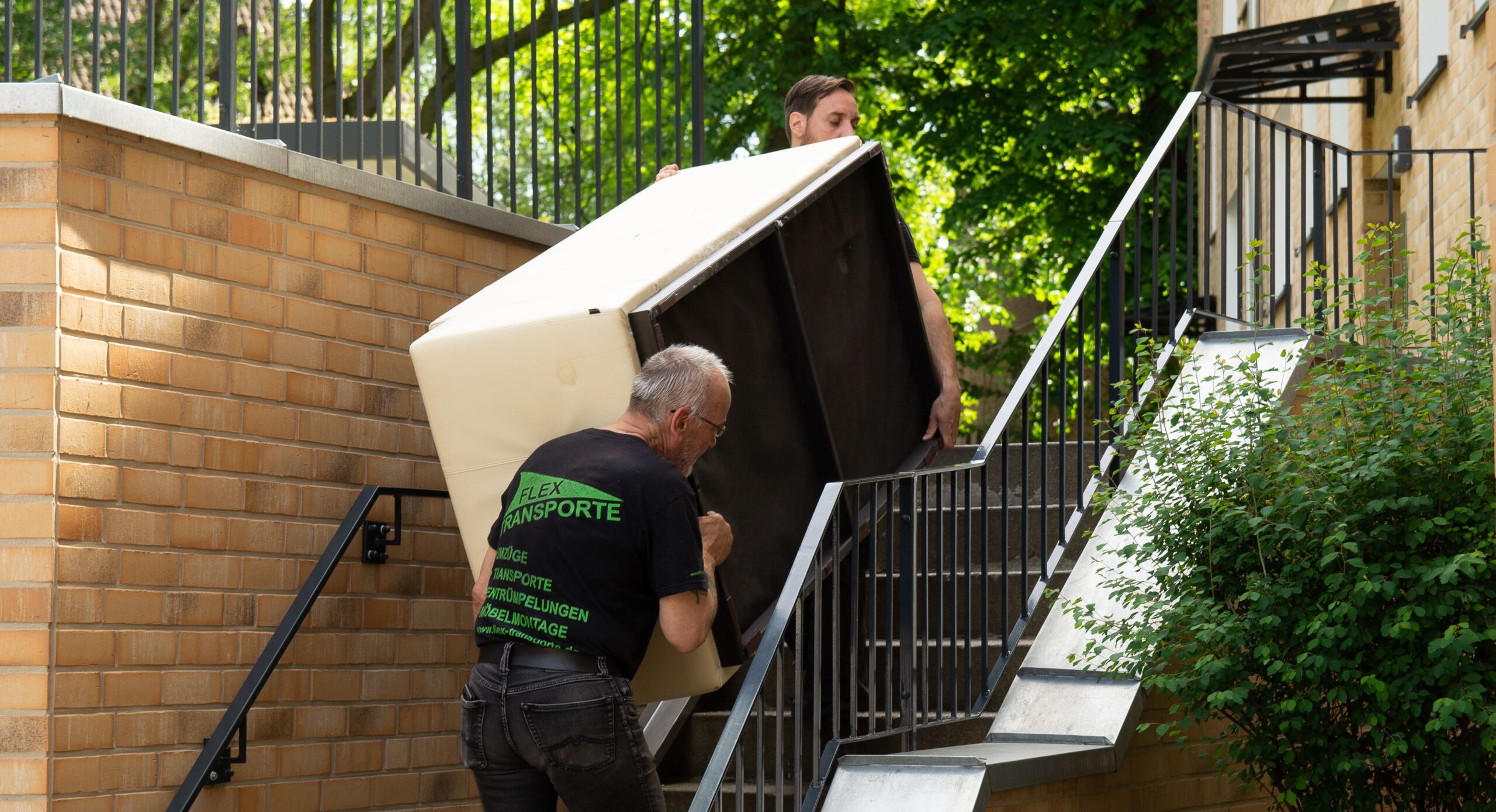 2 Mitarbeiter tragen ein Möbelstück eine Treppe herauf